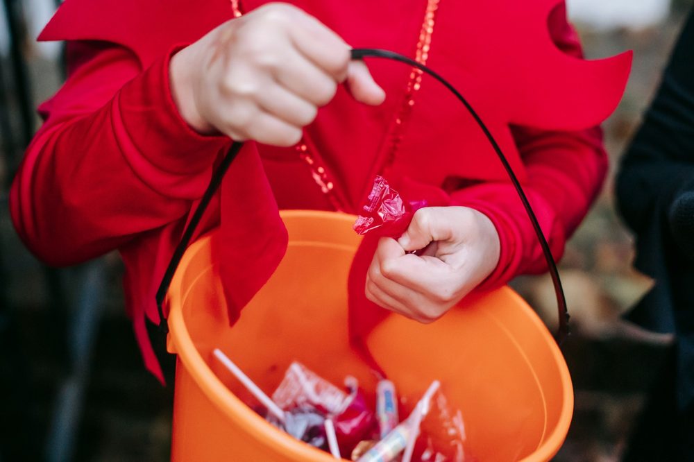 Child in a costume holding a trick-or-treat bucket of candy